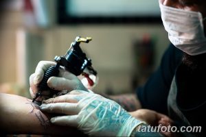 Фото тату процесса нанесения рисунка. Крупный план руки мастера в перчатках и тату-машинки, работающей над кожей клиента.